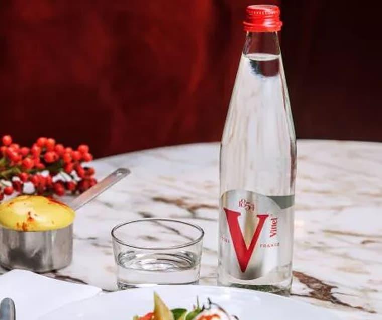 Une salade colorée avec un œuf poché, des carottes, des radis et des légumes verts sur une assiette blanche. À côté, une bouteille d'eau Vittel.