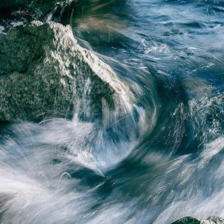 Gentle waves splash against a rugged rock, creating a dynamic interplay of water and texture in a serene natural setting.