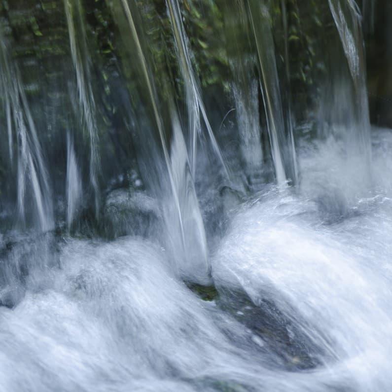 Image floue d'une cascade d'eau ruisselant sur des rochers, créant un effet fluide et serein.
